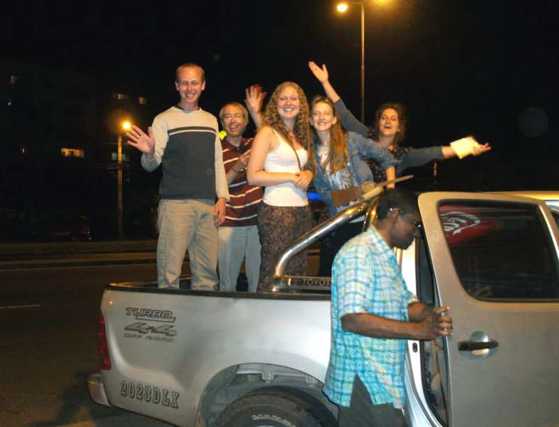 5 people standing and waving in the back of a truck