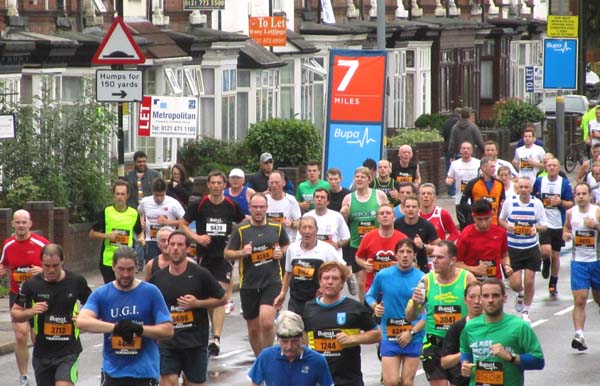 A crowd of runners going along a street lined with houses