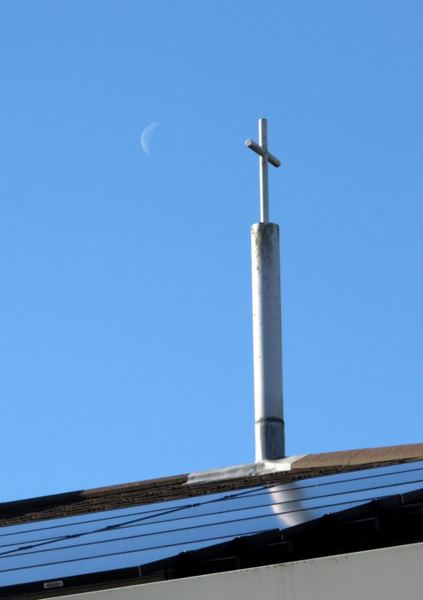 One of our roof-top crosses reflected in the panels, with the Moon behind in the sky