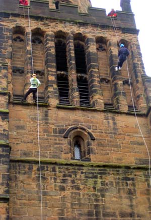 Two people abseiling down a church tower
