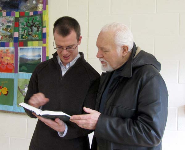 Two men holding an open Bible and discussing it