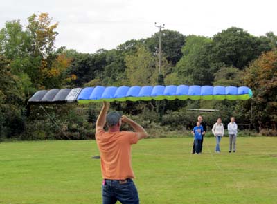 Someone holds a kite while in the distance a group of people hold the rope