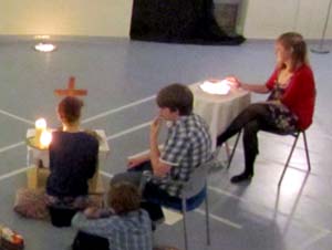 Young people sitting and kneeling at tables with candles and a cross